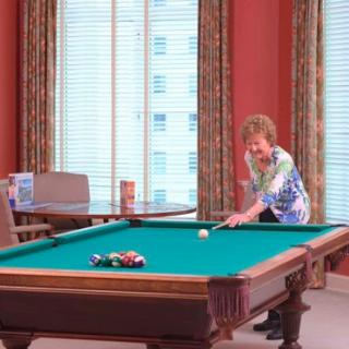 A senior adult focusing on her shot at the pool table in a bright, inviting room.