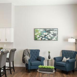 A cozy living room with two blue chairs, a table, and artwork on the wall.