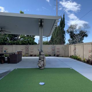A backyard patio featuring a putting green and outdoor furniture under a covered area.
