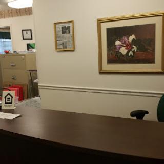 A glimpse of an office reception area featuring a desk, artwork on the walls, and file cabinets in the background.