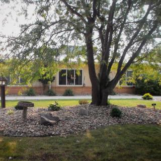 A view of a house with a landscaped front yard featuring a large tree and decorative rocks.