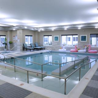 A modern indoor swimming pool with lounge chairs and bright lighting, perfect for relaxation.