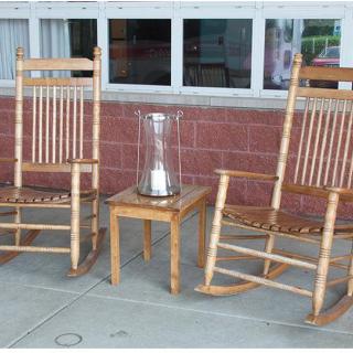 Two wooden rocking chairs with a small table holding a candlestick between them on an outdoor porch.