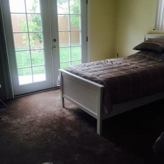A cozy bedroom with a single bed and French doors opening to a garden.