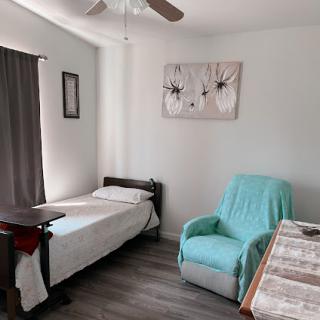 A cozy and minimalistic bedroom setup featuring a single bed, a comfortable chair, and decorative wall art.