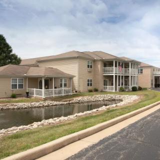 An exterior view of a residential apartment complex with a pond and landscaped surroundings.