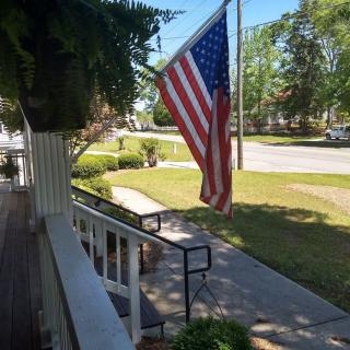 A porch with an American flag overlooking a sunny neighborhood street.