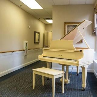 A white grand piano is placed in a well-lit hallway with framed pictures on the walls.