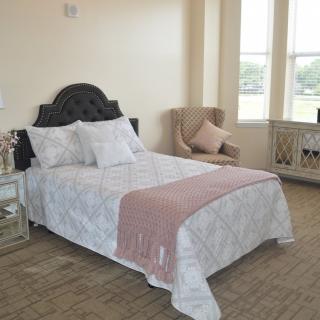 A neatly arranged bedroom with a bed, chair, and large windows.