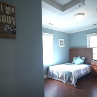 A cozy bedroom with blue walls, featuring a bed with pillows and a bedside table.