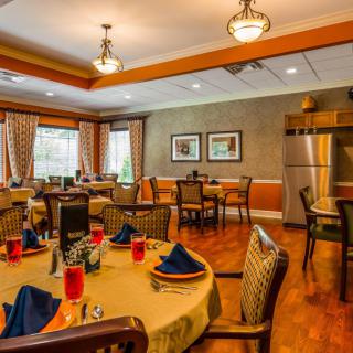 A warmly decorated dining room with neatly arranged tables and chairs, featuring elegant lighting and wooden flooring.