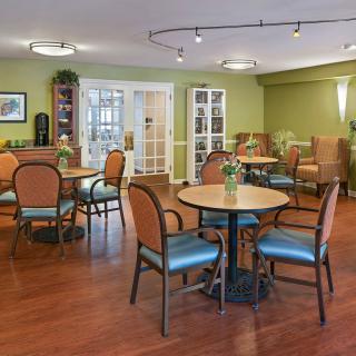 A cozy seating area with tables and chairs, featuring green walls and wood flooring.