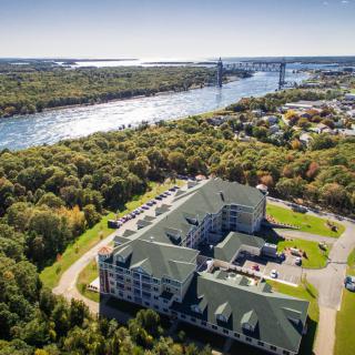 Aerial view of a residential building near a river and bridge surrounded by lush greenery.