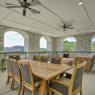 A spacious outdoor patio with wooden dining tables and chairs, featuring stone arches and ceiling fans, offering a scenic view.
