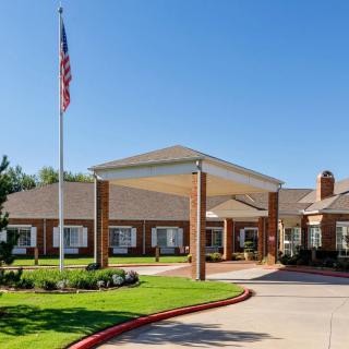 A building with a covered entrance, featuring an American flag and landscaped surroundings.
