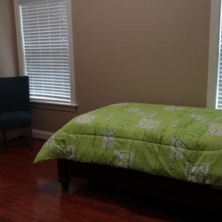 A simple bedroom with a green-bedded bed and a chair by the windows.