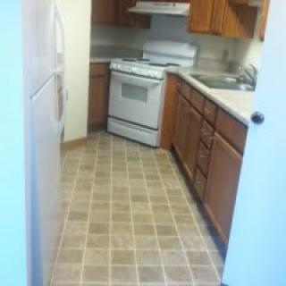 A small kitchen featuring a stove, refrigerator, and wooden cabinets.