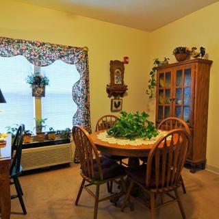 A cozy dining area featuring a round wooden table with chairs, surrounded by a cabinet and window adorned with decorative elements and plants.
