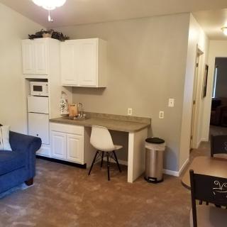 A cozy living area with a kitchenette, featuring a blue sofa and white cabinets.