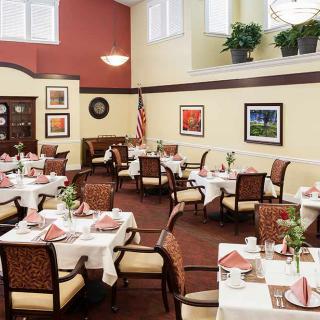 A well-decorated dining room with neatly arranged tables and chairs, featuring artwork on the walls and plants for ambiance.