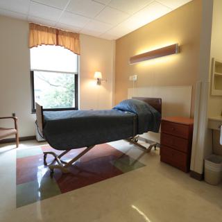 A hospital room with a single bed, window, and furniture.