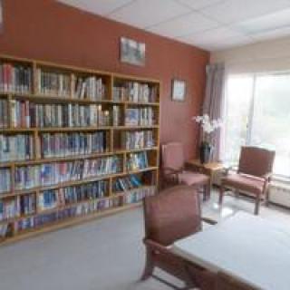 A cozy reading area with bookshelves, chairs, and a table near a large window.