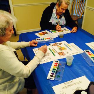 Seniors engaging in a watercolor painting activity at a table.
