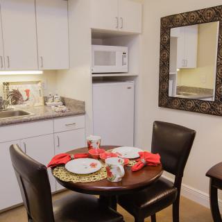 A cozy dining area with a set table next to a compact kitchen, featuring a microwave and refrigerator.