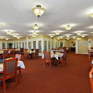 An elegantly furnished dining room with neatly arranged tables and chairs, illuminated by classic lighting fixtures.