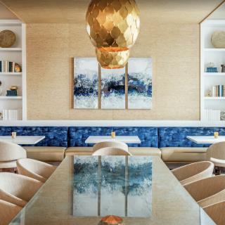 A modern and elegant dining area featuring a large pendant light, contemporary artwork, and plush seating.