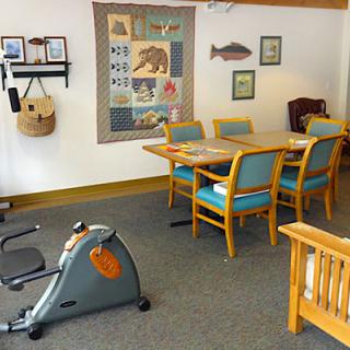 A cozy room featuring an exercise bike alongside a dining area with a table and chairs, adorned with wall art including a quilt.