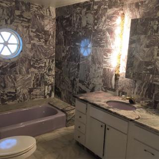A bathroom featuring marble-patterned walls, a lavender bathtub, and a round window.