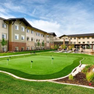 A modern building complex with a small golf putting green in the foreground under a clear blue sky.