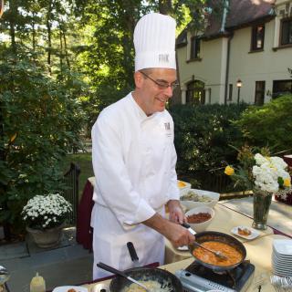 A chef cooking outdoors in a garden setting.