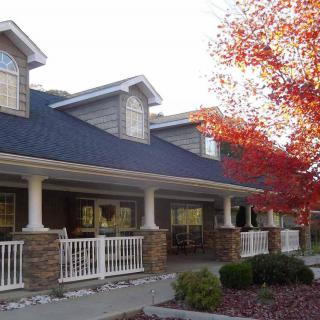 A building with a porch surrounded by autumn foliage and red-leafed trees.