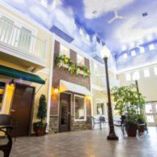 A spacious indoor atrium with a sky-themed ceiling, streetlamps, and lush greenery.