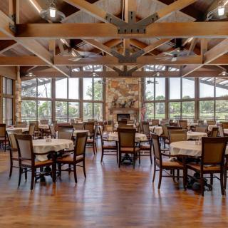 A spacious and well-lit restaurant interior with wooden floors and large windows.