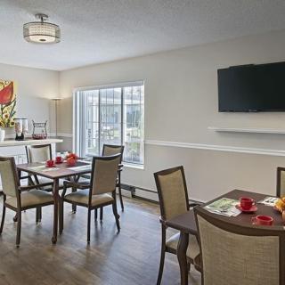 A modern dining room with multiple tables and chairs, a wall-mounted TV, and a large window.