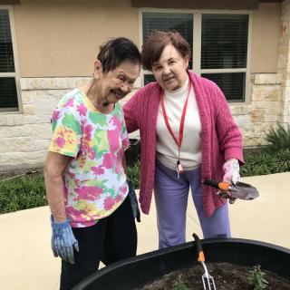 Two elderly women enjoying a gardening activity together outside.