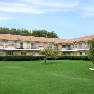 A residential building surrounded by a well-maintained green lawn and trees under a clear blue sky.