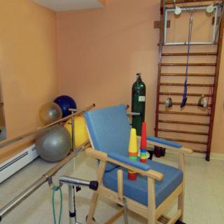 A physical therapy room equipped with various rehabilitation tools, including exercise balls, parallel bars, and an oxygen tank.