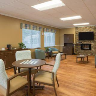 A cozy living room area with modern furniture, including a round table, chairs, and a television mounted above a fireplace.