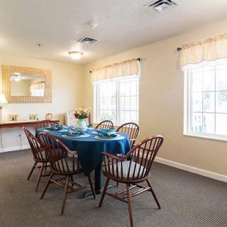 A cozy dining room with a set table, wooden chairs, and natural light from large windows.