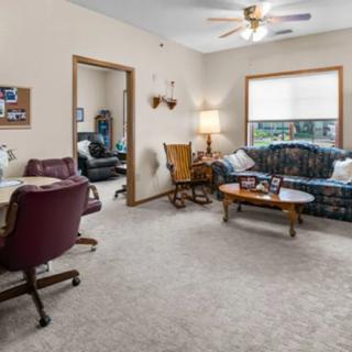 A cozy living room with a sofa, desk, and lamp, featuring carpeted flooring and a window.
