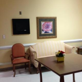 A cozy waiting room with a sofa, chair, and table, decorated with wall art and a television.