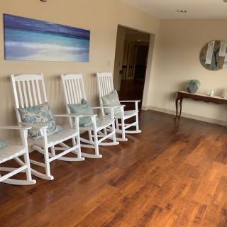 A cozy lobby with white rocking chairs and a wooden floor.