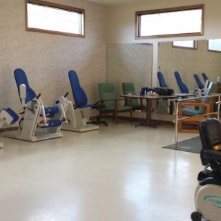 An empty gym with exercise equipment and chairs lined up against the walls.