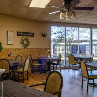 A cozy dining area with natural light streaming through large windows, featuring elegant chairs and tables.