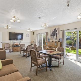 Spacious living room with comfortable seating, a television, and a piano, illuminated by natural light from large windows.