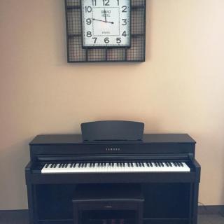A digital piano placed under a wall clock in a music room setting.